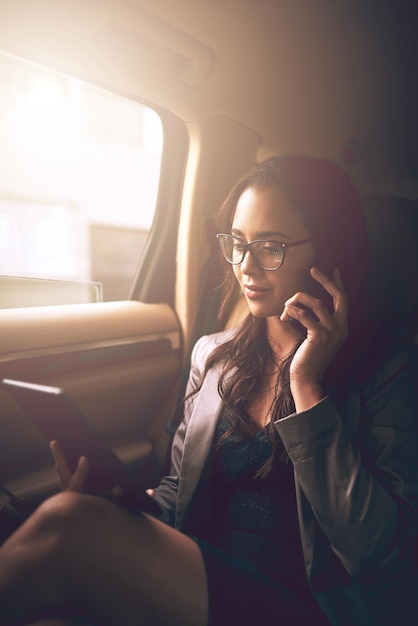 Haar bedrijf vooruit laten gaan Shot van een jonge zakenvrouw die aan het telefoneren is terwijl ze een digitale tablet op de achterbank van een auto gebruikt