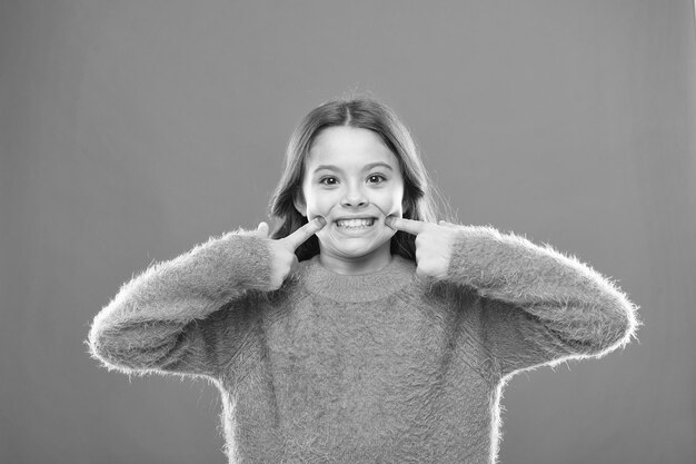 Haar gezonde glimlach gelukkige kinderdag schattig klein meisje glimlachend klein kind herfsttrui voel me comfortabel in casual mode kind oranje achtergrond zorgeloze jeugd ze heeft gezonde tanden