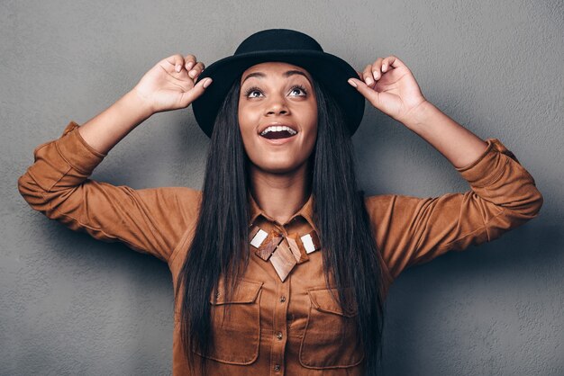 Haar look is zo stijlvol. Mooie jonge vrolijke Afrikaanse vrouw in hoed opzoeken en glimlachen