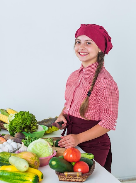 Haar nieuwe hobby verse rauwe groenten tijd om te eten gelukkig kind koken in de keuken gezond en biologisch voedsel alleen vol vitamines kind slijtage chef uniform en hoed tiener meisje maaltijd bereiden