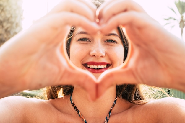 Foto haard en liefdesconcept met jong mooi kaukasisch meisje symboliseert met handen onder het zomerzonlicht