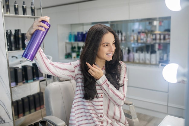 Haarstylen. Langharige jonge brunette die wat haarlak op haar haar uitspreidt