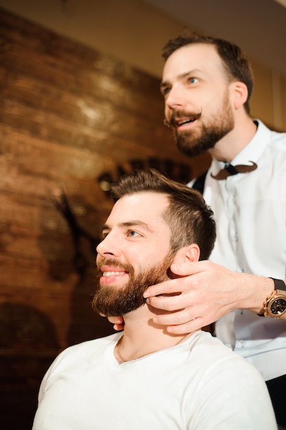 Haarstylist knipt haar en baard van de man in de kapsalon