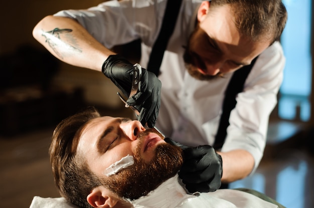 Haarstylist knipt haar en baard van de man in de kapsalon