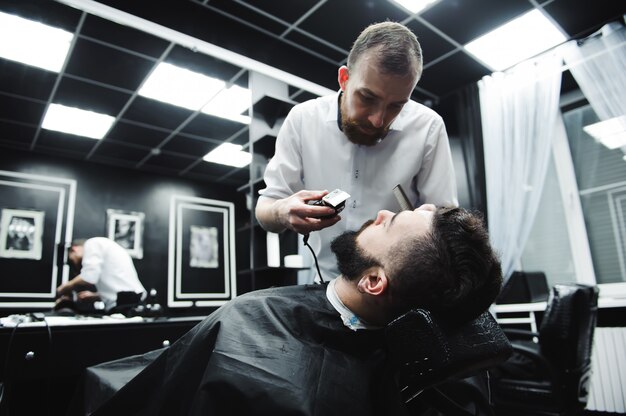 Haarstylist knipt haar en baard van de man in de kapsalon