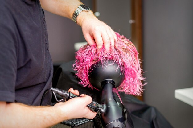 Haarstylist maakt kapsel met behulp van een föhn die op nat, speciaal roze haar blaast in een schoonheidssalon.