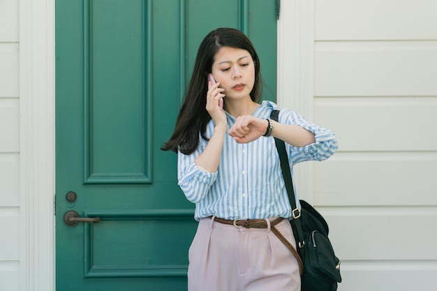 Haast je! Portret van een verantwoordelijke, aantrekkelijke aziatische vrouw die een belangrijke oproep heeft die via een smartphone spreekt en naar een luxe horloge om de pols kijkt. fronsend jong meisje dat op mobiel praat en zegt dat ze snel moet zijn