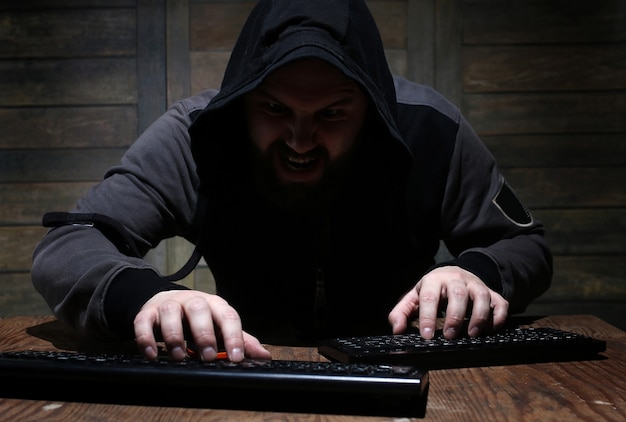 Hacker in the black hood in a room with wooden walls