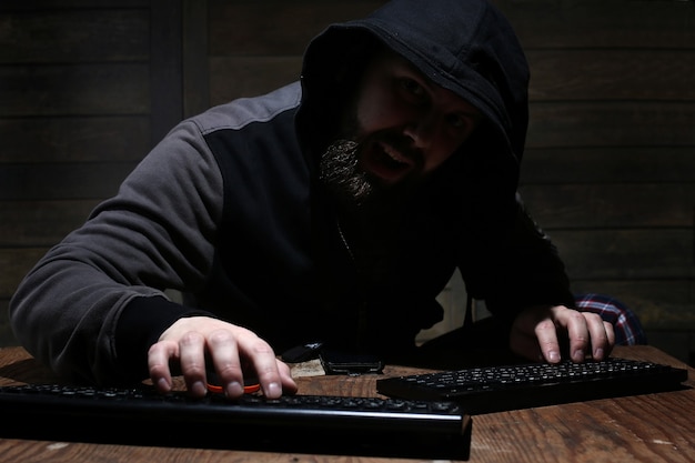 Hacker in the black hood in a room with wooden walls