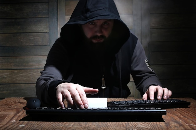 Hacker nel cappuccio nero in una stanza con pareti di legno