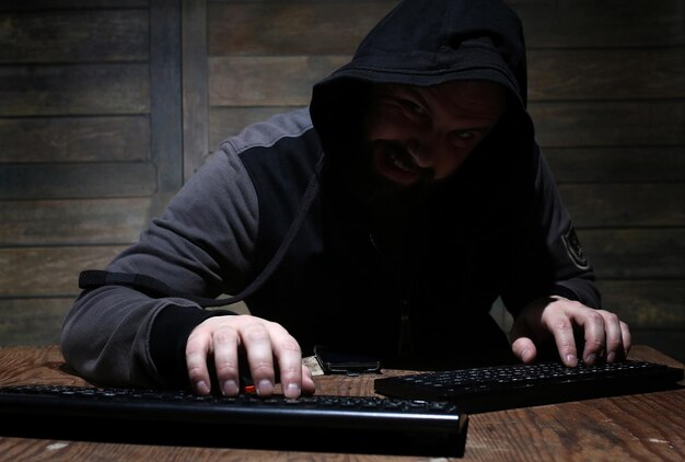 Hacker in the black hood in a room with wooden walls