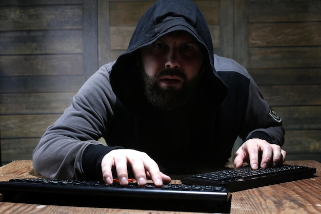 Hacker in the black hood in a room with wooden walls