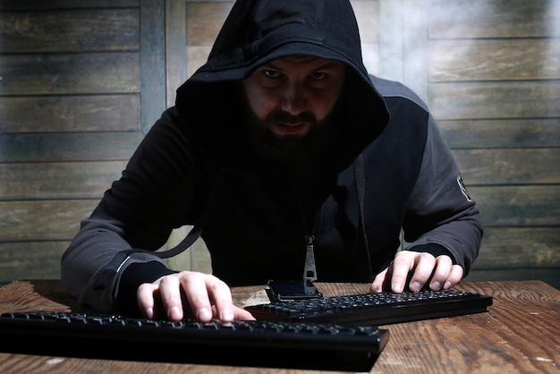 Hacker in the black hood in a room with wooden walls