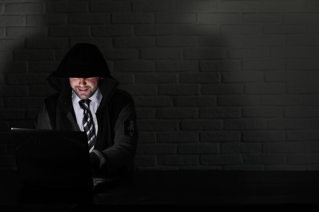 Hacker in black mask and hood at the table in front of the monitor