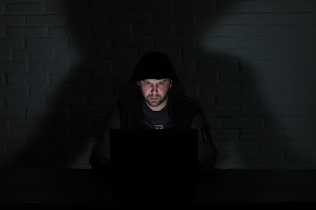 Hacker in black mask and hood at the table