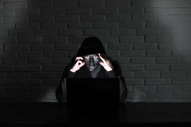 Hacker in black mask and hood at the table