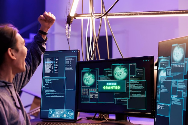 Hacker celebrating access granted to computer system and doing illegal activities. Young asian man raising fist in victory gesture after hacking database successfully in abandoned warehouse