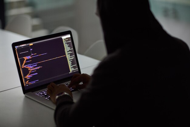 ランサムウェアサイバーセキュリティとフィッシングのためのハッカーコードと人間とラップトップ画面を使用したプログラミング夜間の詐欺ネットワークシステムとデータを入力するプログラマーによるコーディング技術と犯罪