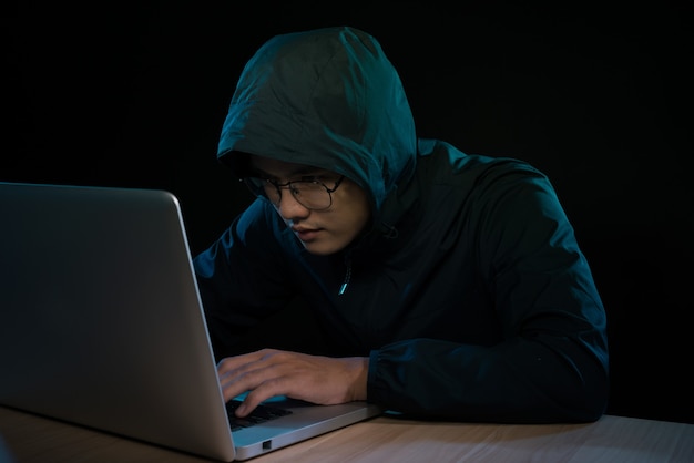 노트북 앞에 앉아 있는 어두운 후드티를 입은 해커. 컴퓨터 개인 정보 공격