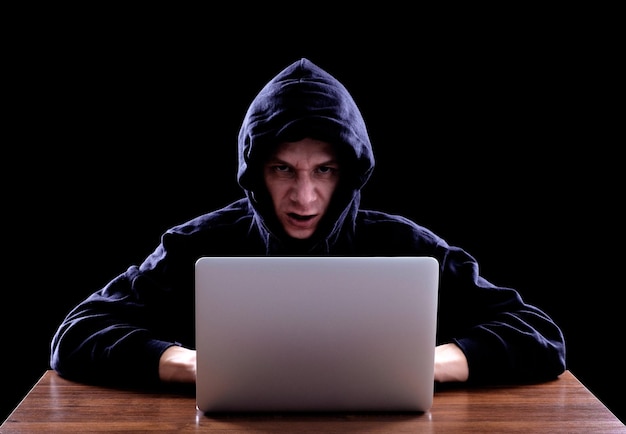 Hacker in a dark hoody sitting in front of a notebook Cybersecurity concept Dark background