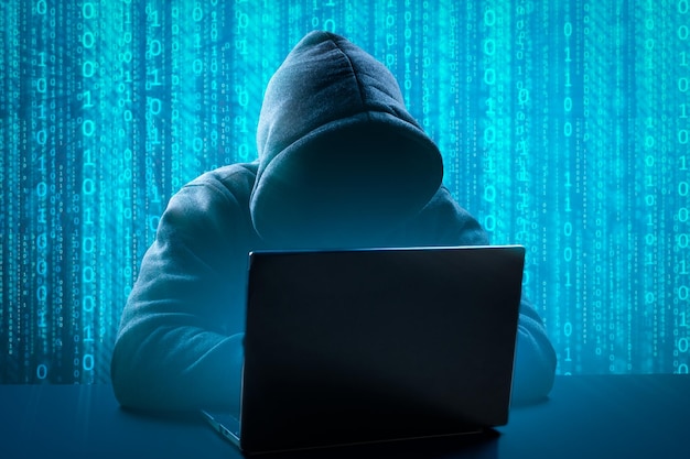 Hacker die computerlaptop gebruikt voor het organiseren van een massale aanval op gegevensinbreuken op bedrijfsservers ondergrondse geheime locatie Anonieme persoon in de kap zit achter de computer die met laptop werkt
