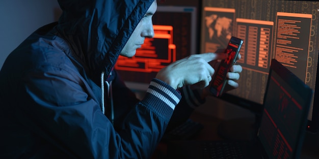 Hacker in the hood is pointing his finger at the display indicating the location of the cyberattack in neon light