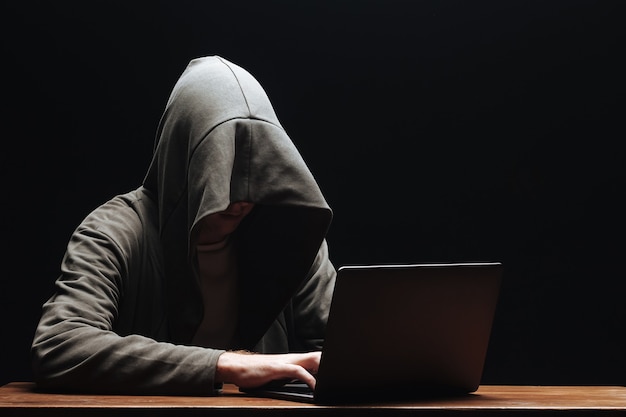 Hacker in una cappa con un laptop su uno sfondo nero