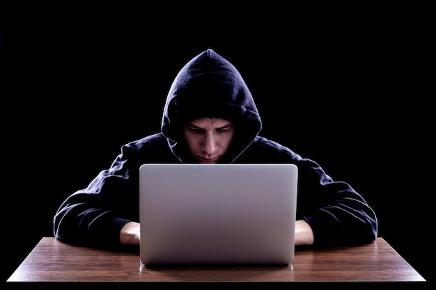 Hacker in een donkere hoody zit achter een laptop