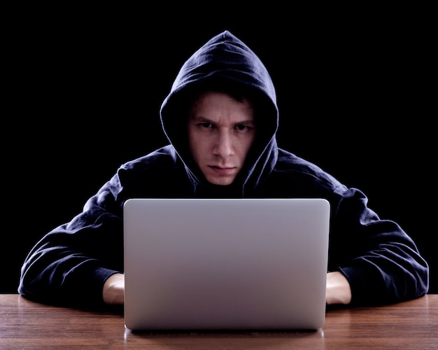 Hacker in een donkere hoody zit achter een notebook