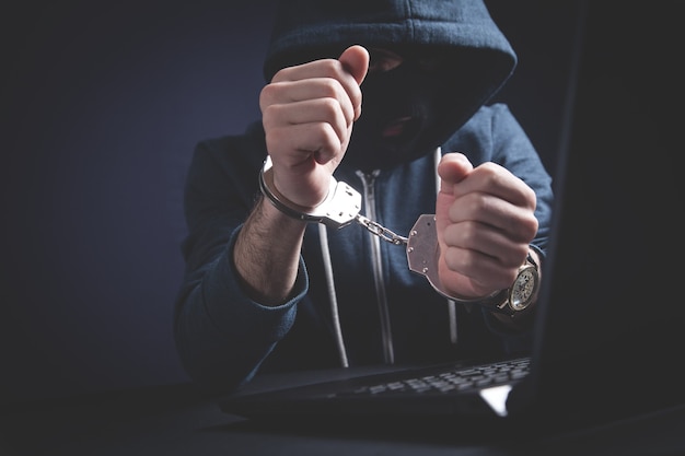 Hacker in handboeien met laptop. Cybercriminaliteit