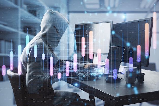Hacker in hoodie met een computer op het bureau in een wazig kantoorinterieur met creatieve gloeiende bedrijfsgrafiek en kaart Globale investering diefstal en malware concept Dubbele blootstelling