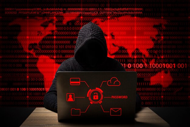 Hacker in a jacket with a hood with a laptop sits at the table