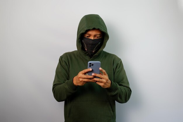 Хакер, смотрящий на экран телефона, одетый в пушистый и зеленый капюшон, изолированный на белом фоне