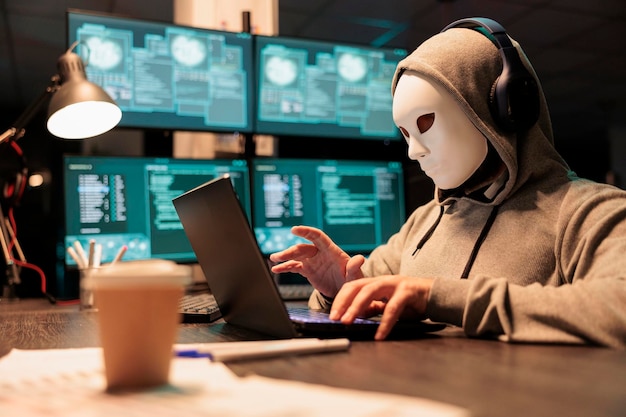 Hacker met masker en capuchon die beveiligingsserver doorbreekt, virus installeert om computermalware te maken en grote online gegevens te stelen. Gemaskerde criminele oplichter die 's nachts het netwerksysteem hackt.