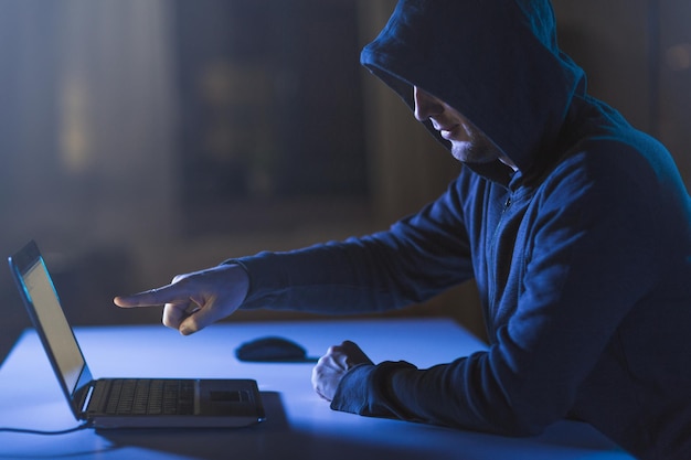 暗い部屋でラップトップ コンピューターを指しているハッカー