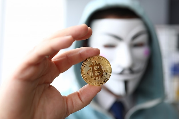 Photo hacker wear anonymus mask hold bitcoin in hand