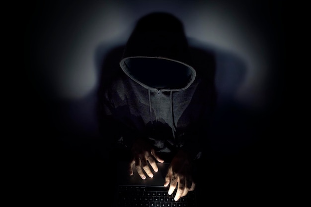 Фото Хакер с капюшоном использует компьютер в темноте