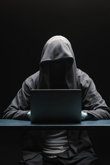 Hacker without a face in a hood with a laptop on a black background