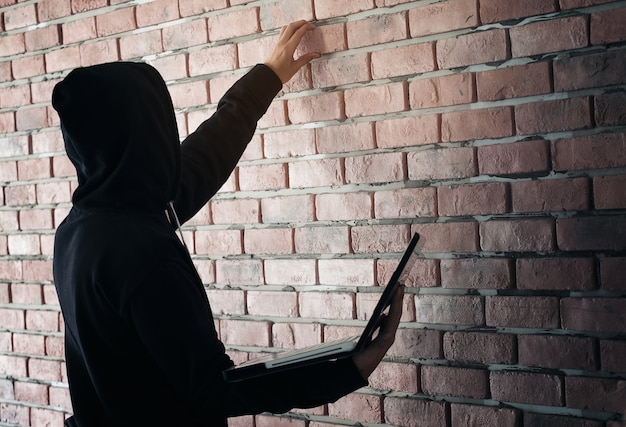 Hacker working on his computer. Black masked hacker in the black long sleeve shirt is lapt