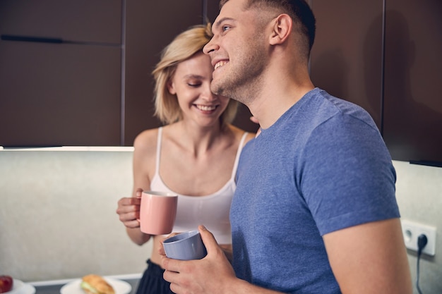 Photo hadsome sporty male relaxing with  blond woman while drinking tea and communicating at home