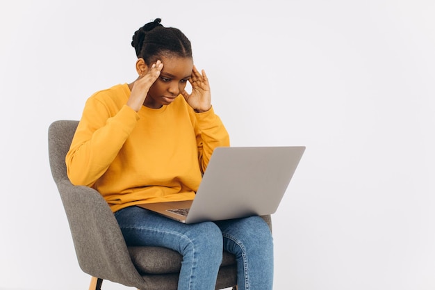 HAfrican American woman sitting on a chair, talking on a video call and she is shocked.