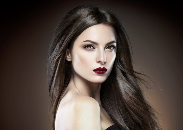 髪の美しさの女性の長いブルエット滑らかな美しいマニキュアネイルモデル赤い口紅茶色の背景夜のメイクの肖像画。スタジオショット。