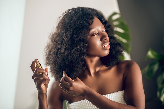 Уход за волосами. Привлекательная афро-американская женщина распыляет сыворотку на волосы