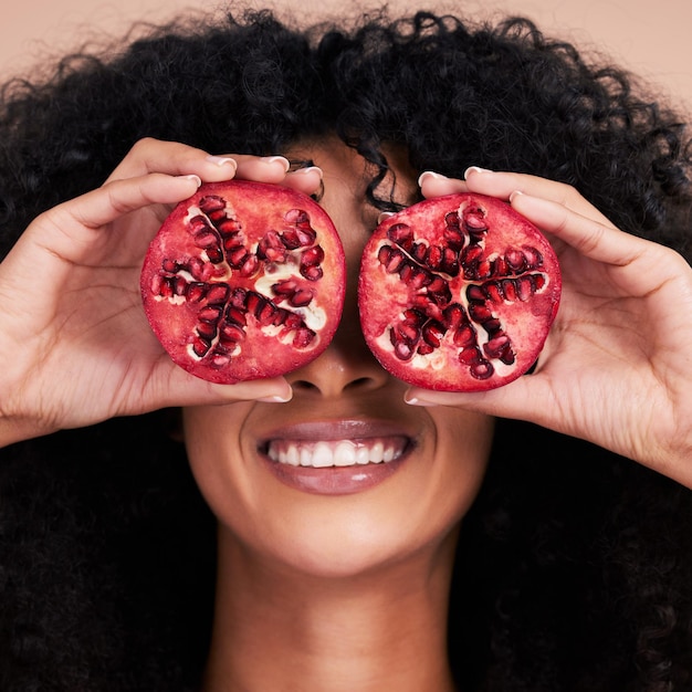 Hair care face and black woman with pomegranate in studio isolated on a brown background Fruit skincare and happy female model holding food for healthy diet nutrition or vitamin c and minerals
