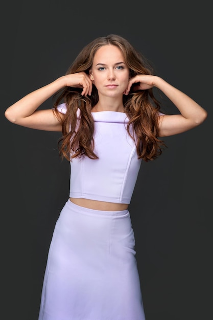 Hair care and fashion women's beauty A young girl holds her hands behind her head while standing lavender dress looking at the camera