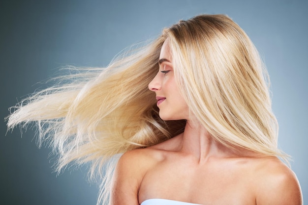 Foto cura dei capelli donna sana e bionda con cheratina per la crescita benessere e volume su uno sfondo blu da studio modello di lusso felice e ragazza con un sorriso per il trattamento dei capelli bellezza e cura