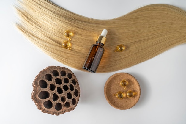 Un olio o un siero per la cura dei capelli in un flacone contagocce marrone e capsule dorate che giacciono su un mockup di marketing di prodotti per capelli biondi