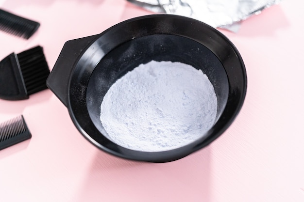 Hair color dye powder in a black plastic mixing bowl on a pink background.