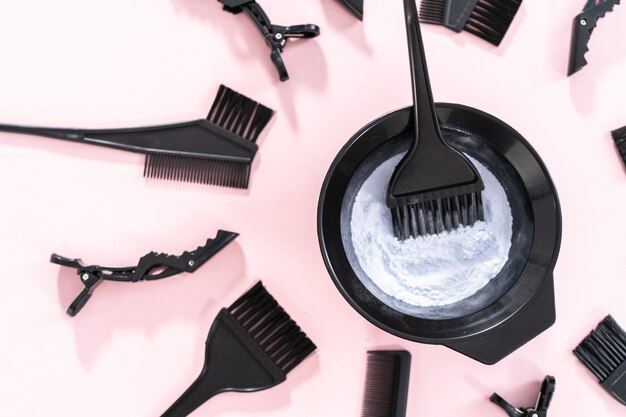 Hair color dye powder in a black plastic mixing bowl on a pink background.