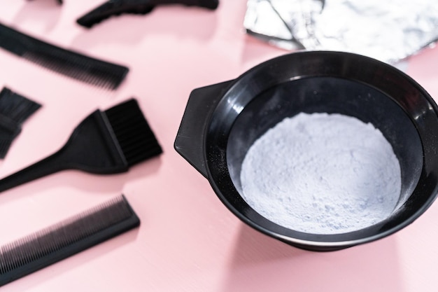hair color dye powder in a black plastic mixing bowl on a pink background.